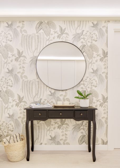 Consola negra con espejo redondo, decorada con una planta y fondo de papel pintado floral.