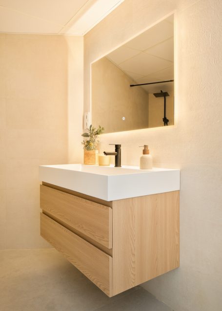 Baño moderno con lavabo flotante y espejo iluminado, decorado con plantas.