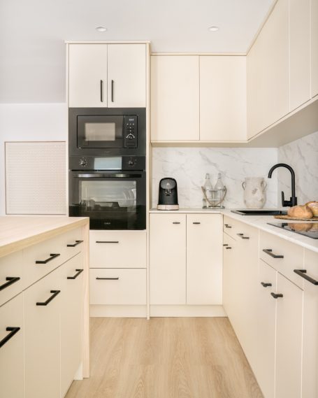 Cocina moderna con armarios claros, electrodomésticos y encimera de mármol.