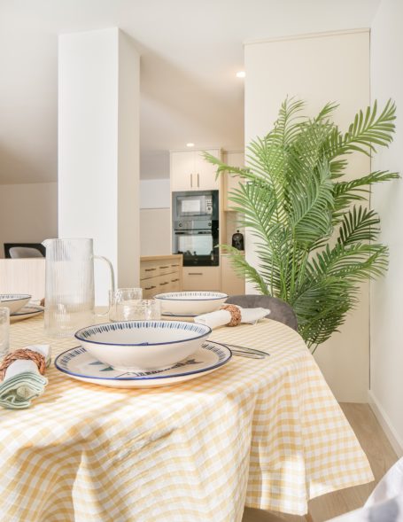 Mesa bien servida con mantelería amarilla y una planta decorativa al fondo.