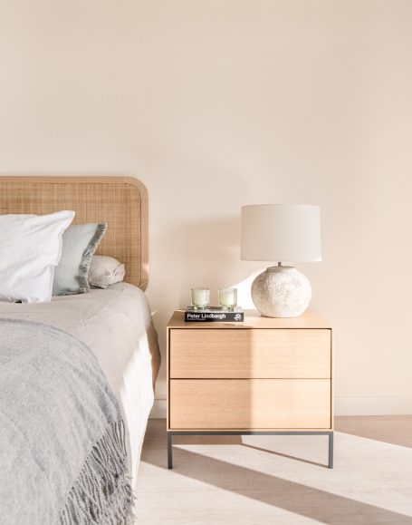 Cama con cabecera de mimbre y mesita de noche con lámpara y decoraciones.