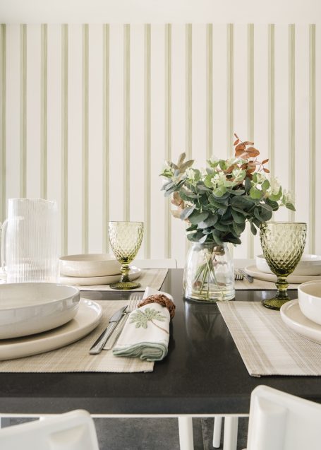 Mesa elegantemente decorada con platos, copas y un jarrón de flores. Fundo de rayas suaves.