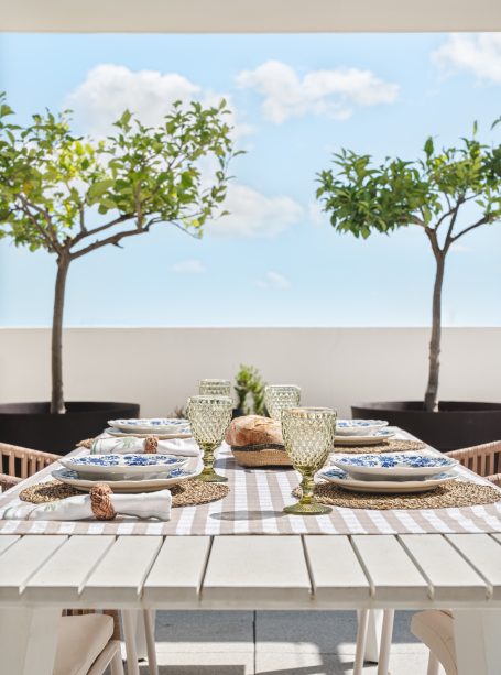 Mesa de comedor con mantelería a rayas y vista al cielo y árboles en el fondo.
