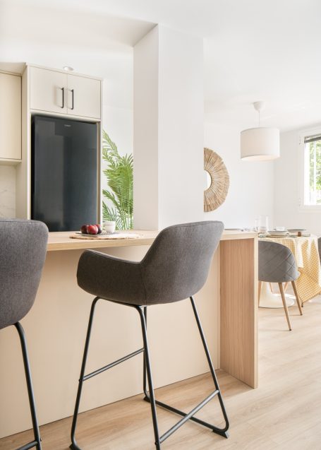 Barra de cocina con taburetes grises y decoración minimalista en un entorno luminoso.