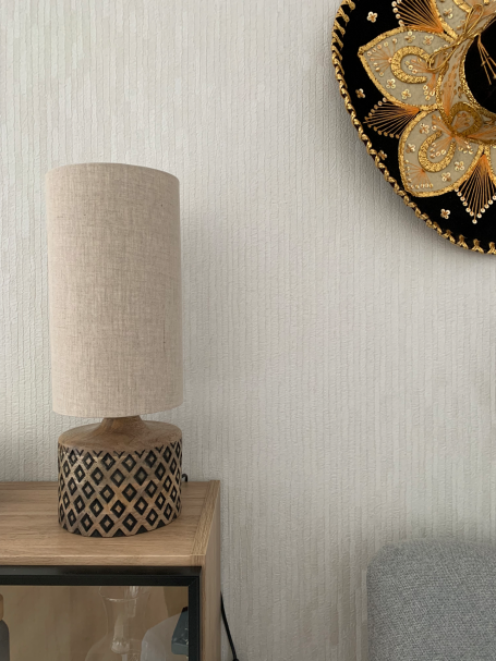 Lámpara de mesa con base de madera decorativa y pantalla de tela sobre una mesa.