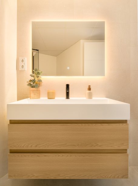 Baño moderno con lavabo de madera, espejo iluminado y decoración minimalista.