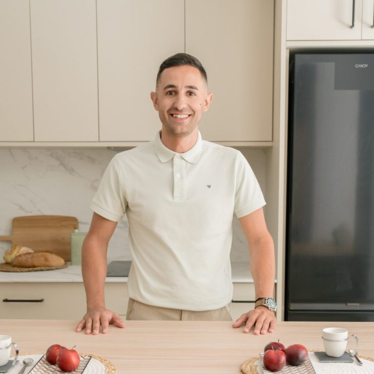 Hombre caminando por un jardín con árboles rojos y vegetación variada.