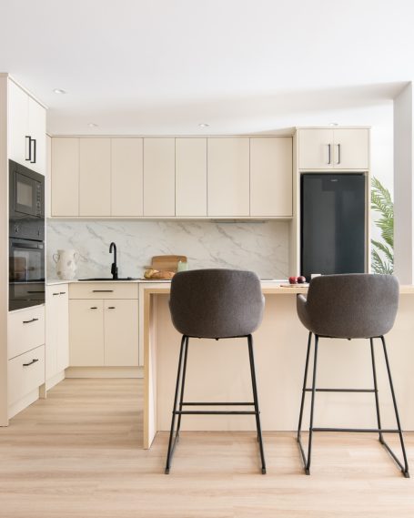 Cocina moderna con armarios claros, barra y taburetes oscuros.