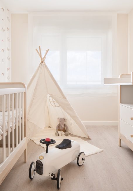 Habitación infantil con cuna, tipi, juguete de coche y ventana iluminada.